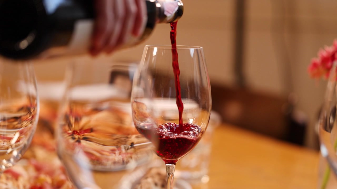 Primer plano de vino tinto sirviéndose en una copa sobre una mesa de restaurante cálida y con poca luz.