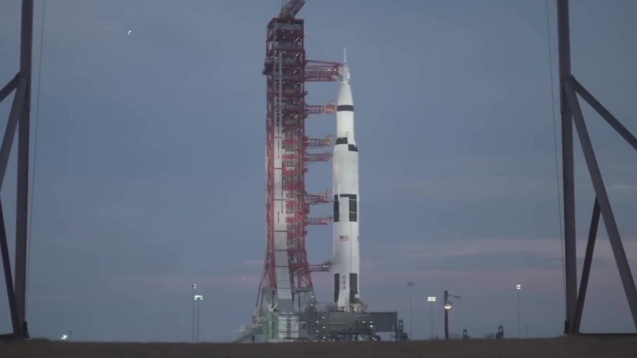 Static shot of massive Saturn V rocket standing on the launch pad at dawn.