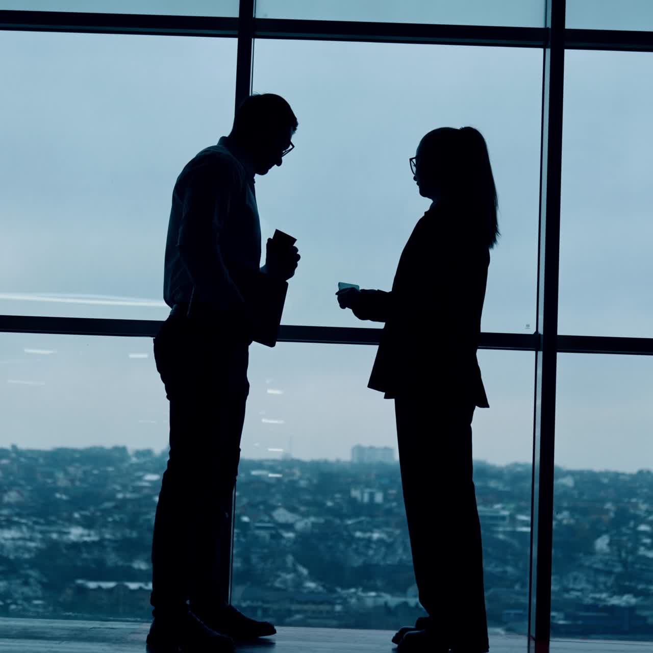 Sagome scure di uomo e donna sono in piedi alla finestra panoramica. Conversazione tra colleghi in ufficio. Vista dal basso.