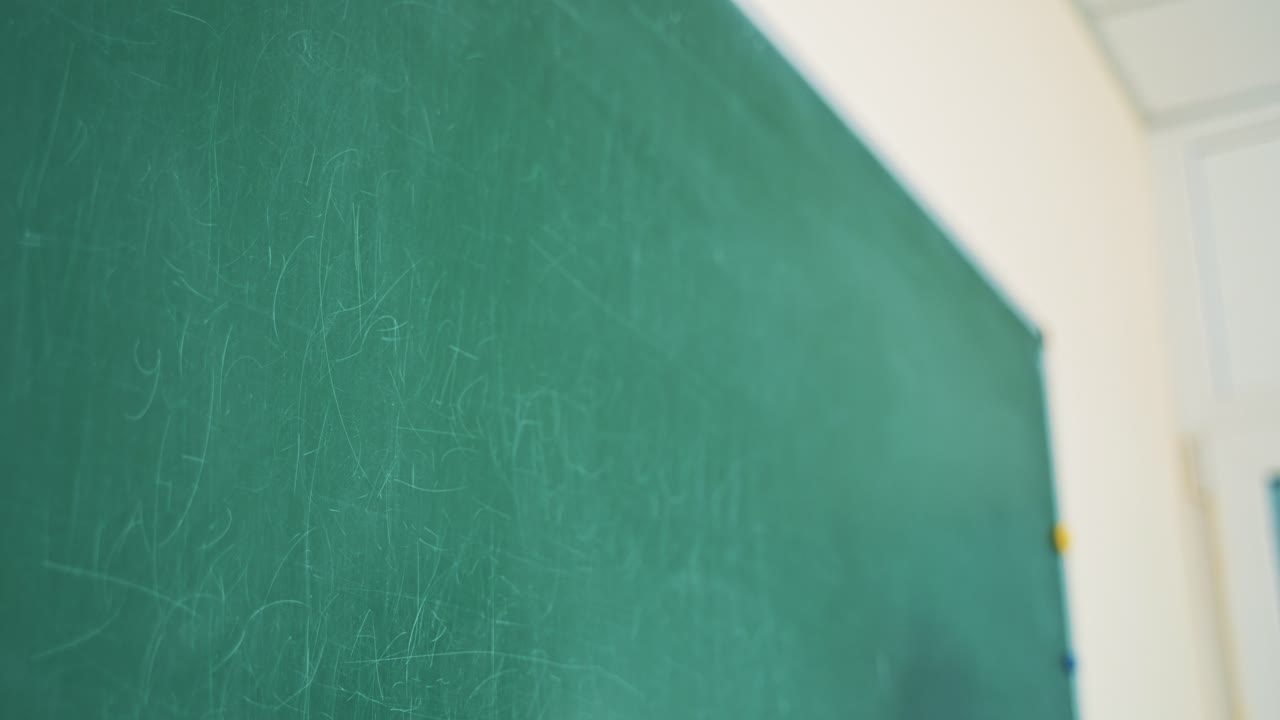 Close-up teacher's hand effaces the chalk from the blackboard. Woman wiping the written English words with a sponge on board in the classroom indoors.