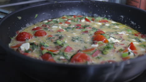 slow pan sliding shot right to left of tomato, red pepper, kale, zucchini- courgette, bacon and onion omelette frittata cooking in frying pan