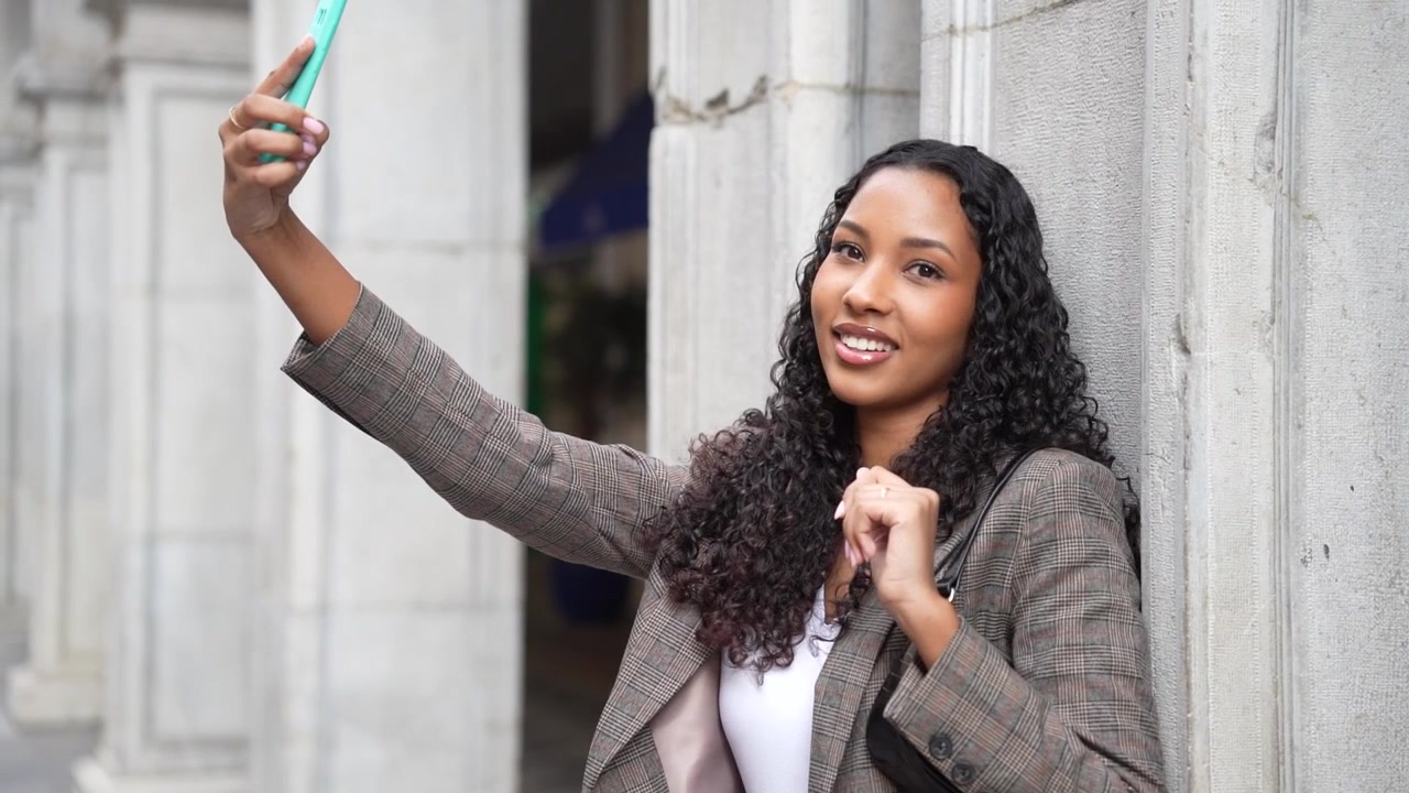 A young woman happily taking a selfie in a vibrant urban setting with a colorful cloak