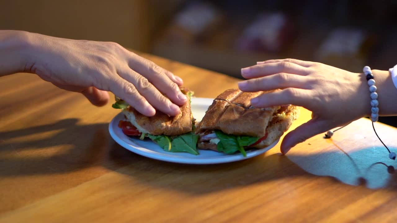 un par de manos tomando un sándwich de baguette en una mesa a media cámara lenta.