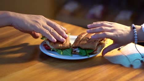 un par de manos tomando un sándwich de baguette en una mesa a media cámara lenta.