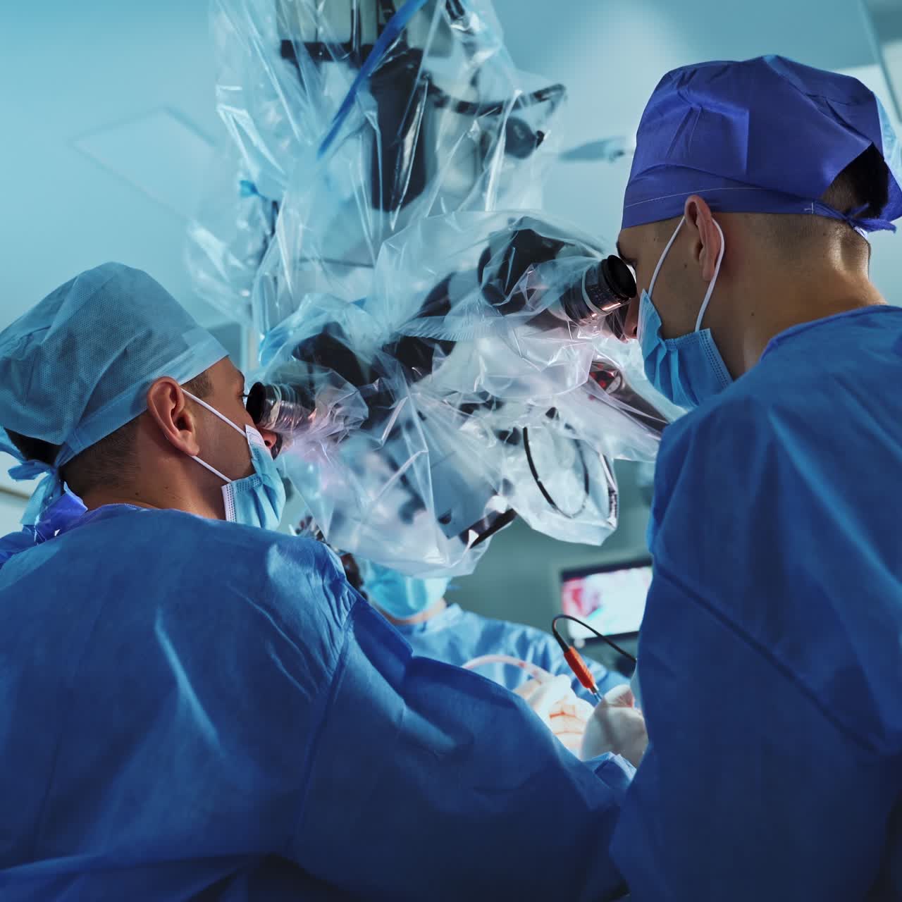 Attentive focused neurosurgeons perform operation looking into microscope. Low angle view on the doctors using technology at surgical procedure