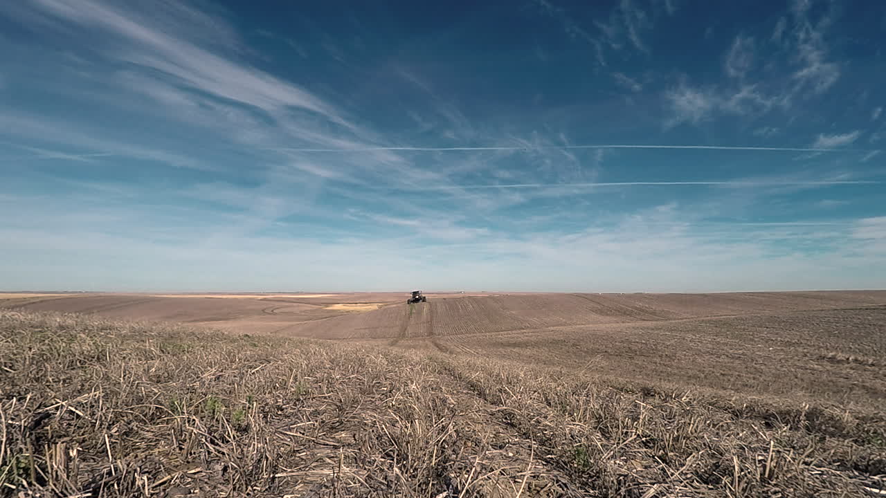 Klar blå himmel over en kørende landbrugstraktor med sprøjte, der anvender ukrudtsmidler på markerne.
