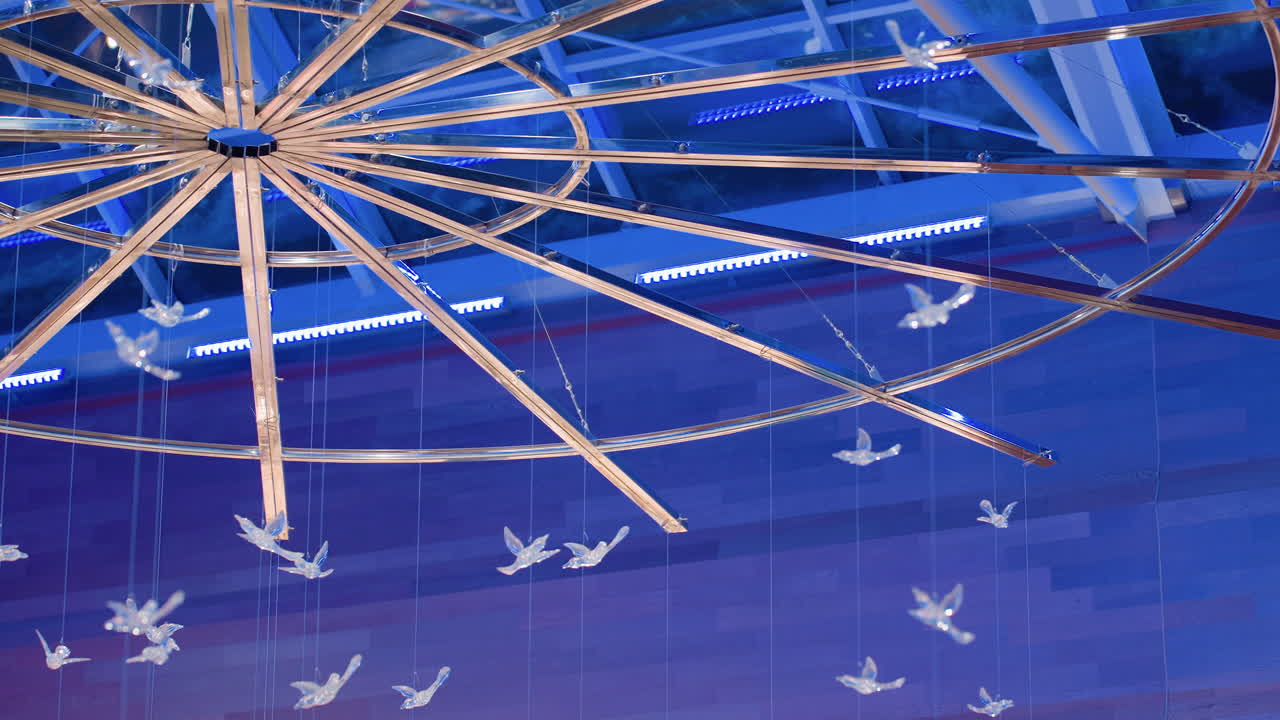 Artistic ceiling interior design showing suspended crystal birds under circular frame illuminated with soft blue light inside modern building creating elegant decorative atmosphere