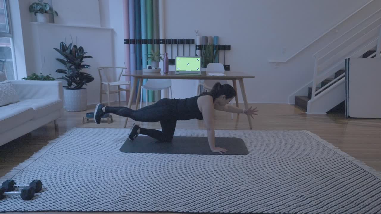 una mujer haciendo estiramientos frente a una computadora mientras está en casa en su sala de estar