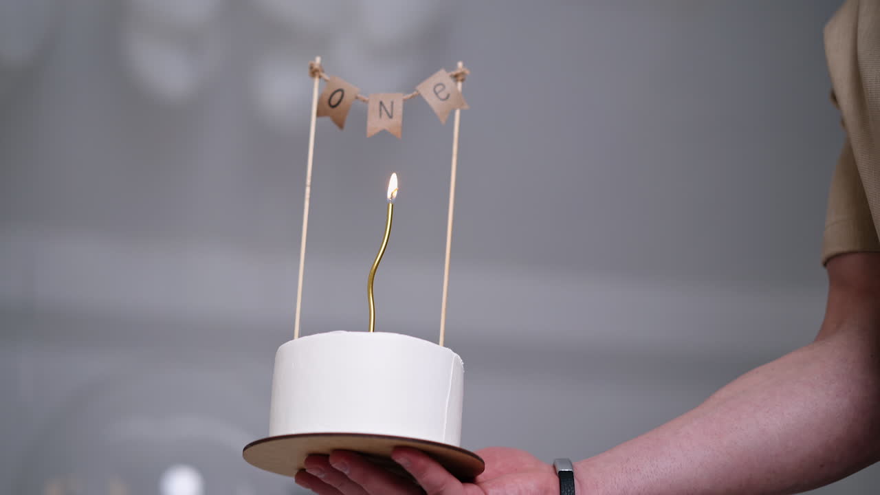 Male hand holding a beautiful birthday cake for one year. Celebration of first year of life or anniversary. Low angle view.
