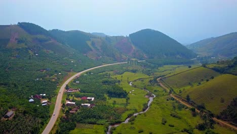 high-altitude aerial view of winding road with cars passing through a lush green valley surrounded by hills and farmland in western uganda, highlighting rural transportation infrastructure