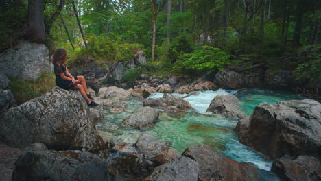 4k uhd cinemagraph - seamless video loop of a young brunette woman sitting at a river at the scenic mountain lake hintersee in bavaria, germany