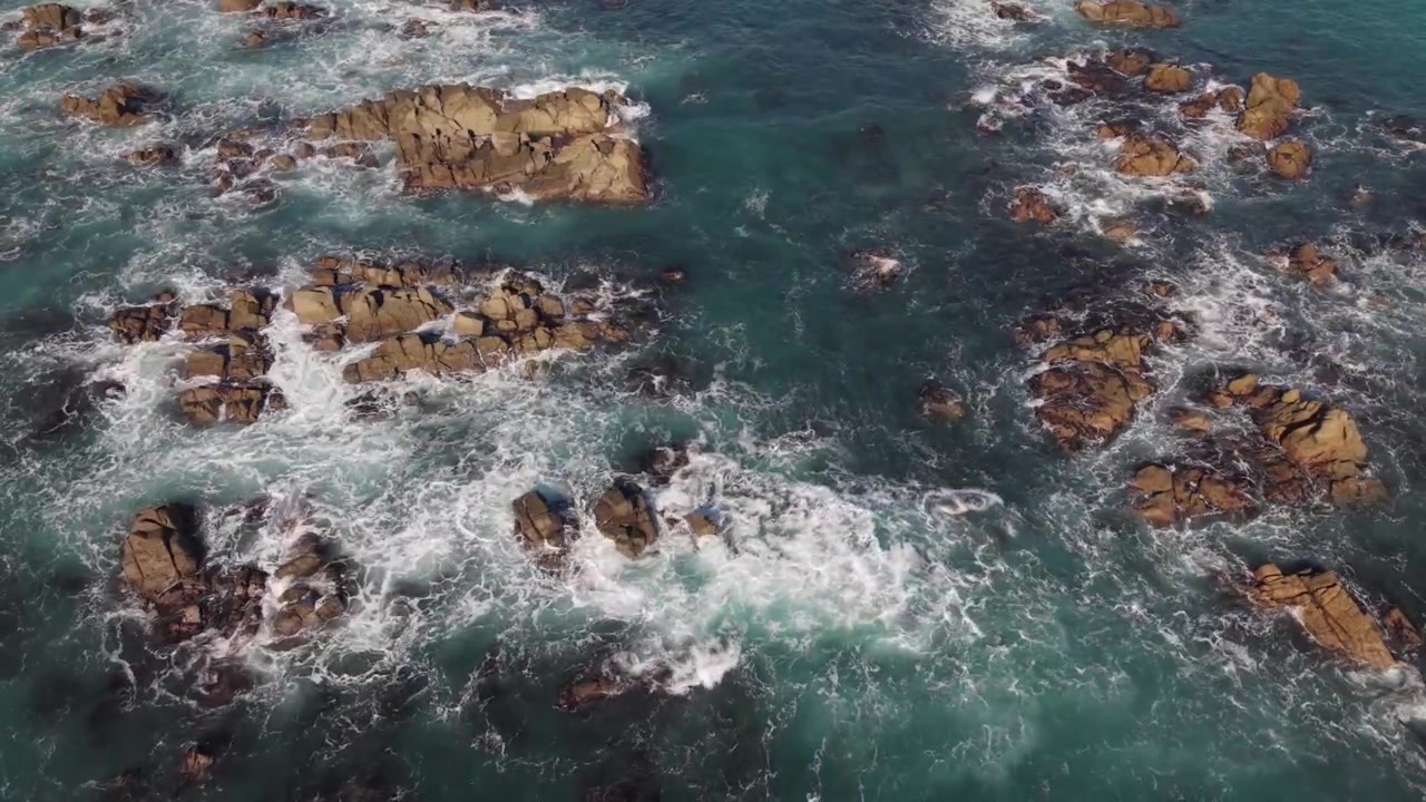 Riprese statiche con drone dall'alto di affioramenti rocciosi sotto il sole del tardo pomeriggio con onde che si infrangono sulle rocce in un mare azzurro e limpido e viste sul fondale marino.