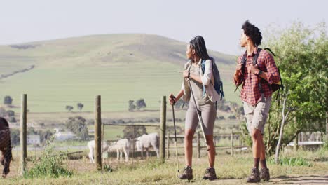 Happy-african-american-couple-with-backpacks,-hiking-with-trekking-poles-together,-slow-motion