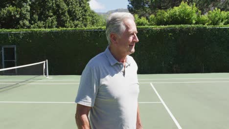 Porträt-Eines-Kaukasischen-älteren-Mannes,-Der-Lächelt,-Während-Er-Auf-Dem-Tennisplatz-Steht