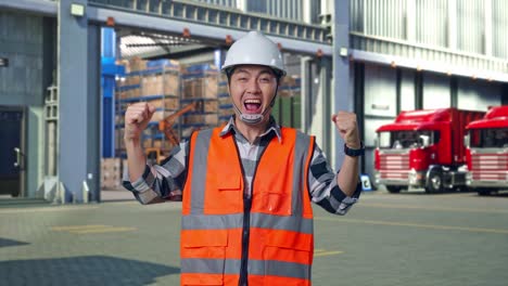 Asian Male Engineer With Safety Helmet Screaming Goal Celebrating Working , Outside of Logistics Distributions Warehouse