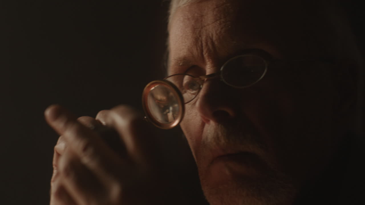 Older passionate man evaluates an old silver skull watch in his office at night