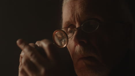 older passionate man evaluates an old silver skull watch in his office at night