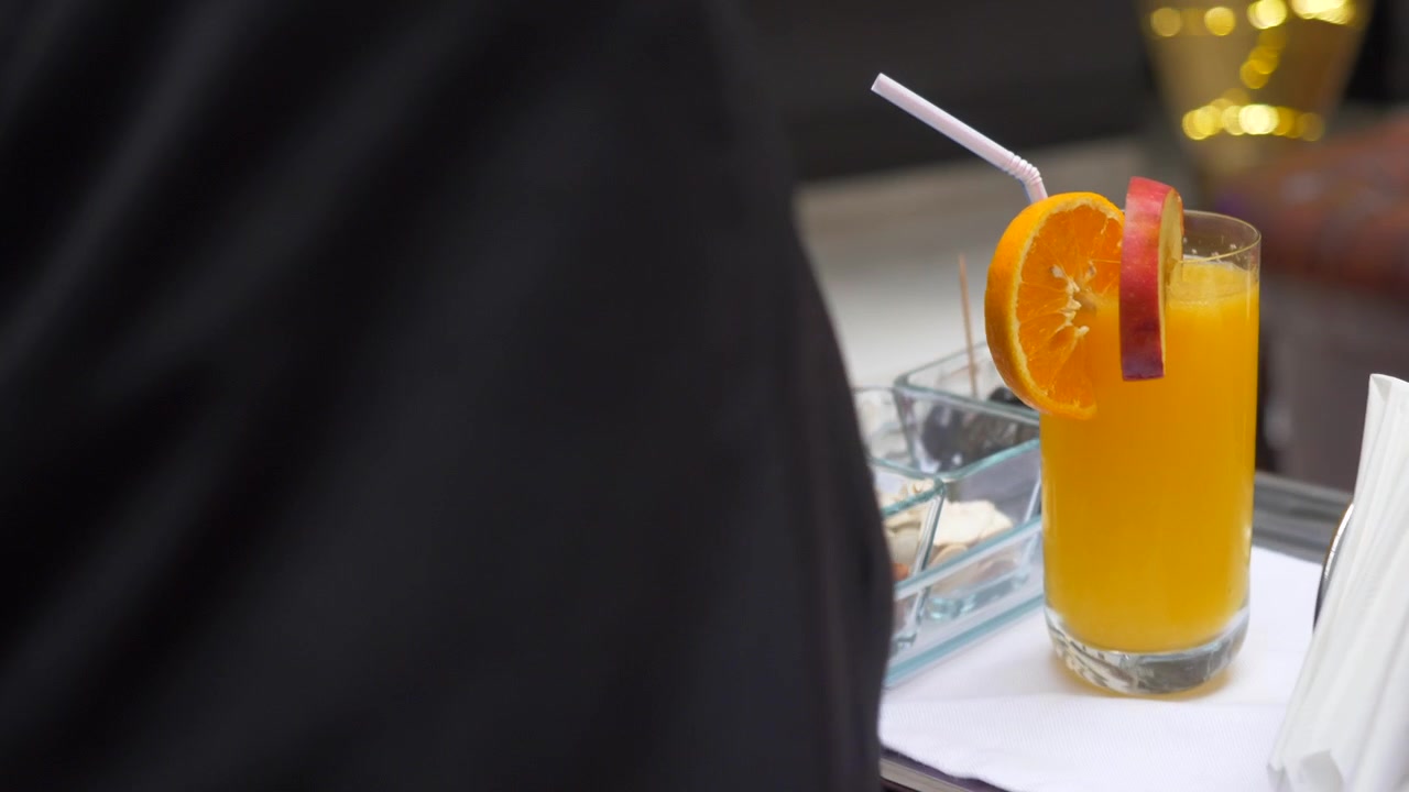 Una persona che porta una tazza di succo d'arancia con mandorle e tovaglioli su un vassoio, carrellata.