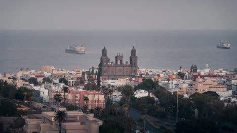 day to night timelapse of las palmas, featuring the cathedral of santa ana, colorful buildings, palm trees, and an ocean view with a passing ship. ideal for tourism, urban, and cultural projects.
