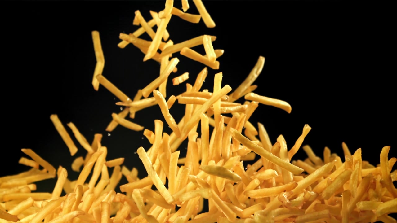 Patatine fritte dorate che cadono al rallentatore su sfondo nero
