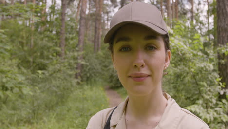 close-up view of caucasian female forest warden wearing cap and looking at camera with crossed arms in the woods