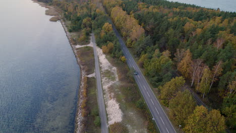 Car-driving-on-a-coastal-road-with-autumn-foliage-and-calm-sea-at-dusk