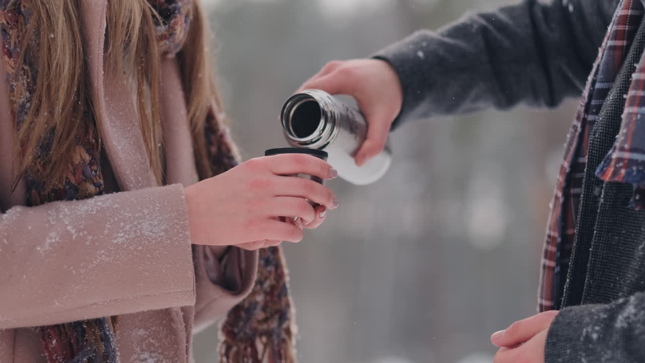 una pareja amorosa, hombre y mujer, en el bosque invernal bebiendo té de un termo. hombre y mujer con estilo con un abrigo en el parque en invierno para dar un paseo. camara lenta