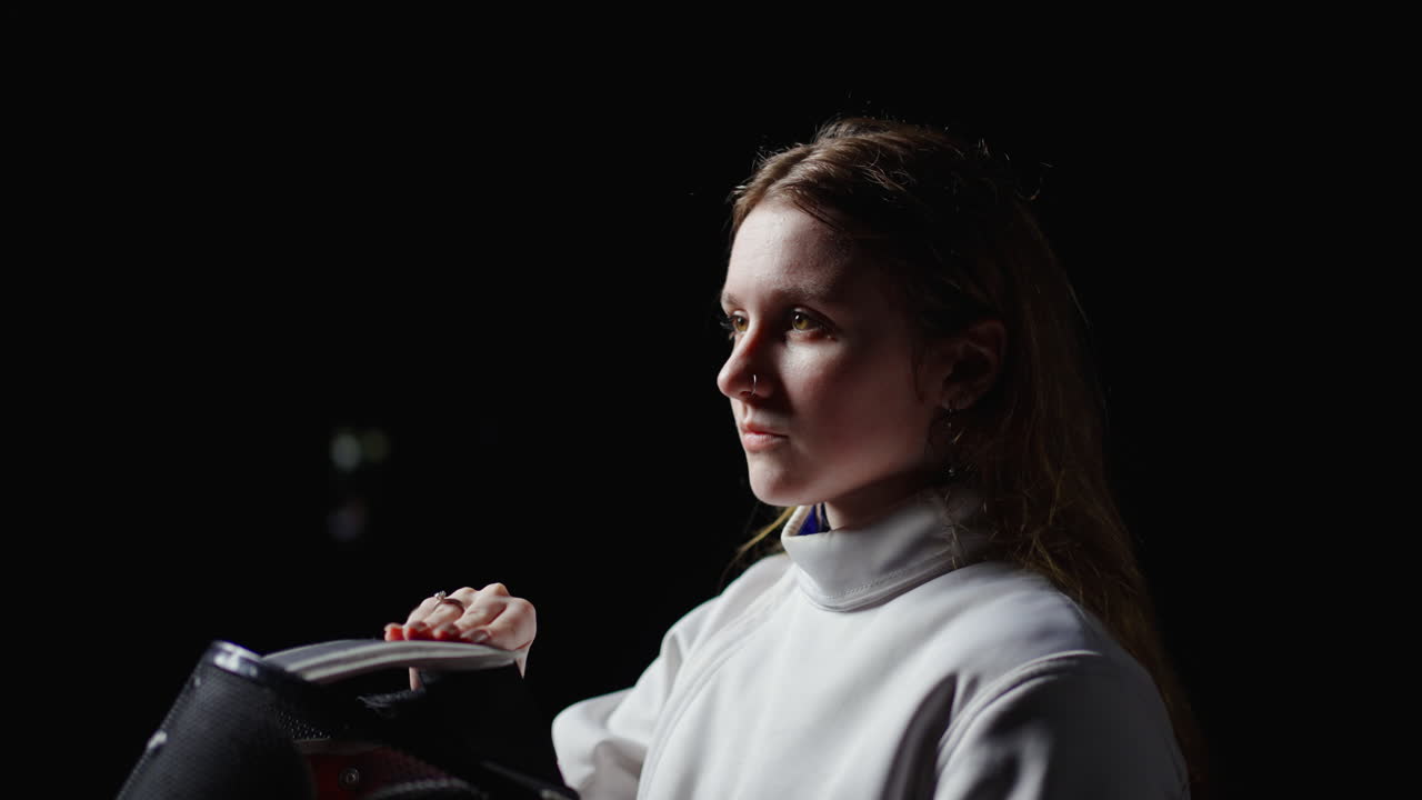 una mujer joven con una máscara de esgrima y uniforme, preparándose para un partido.