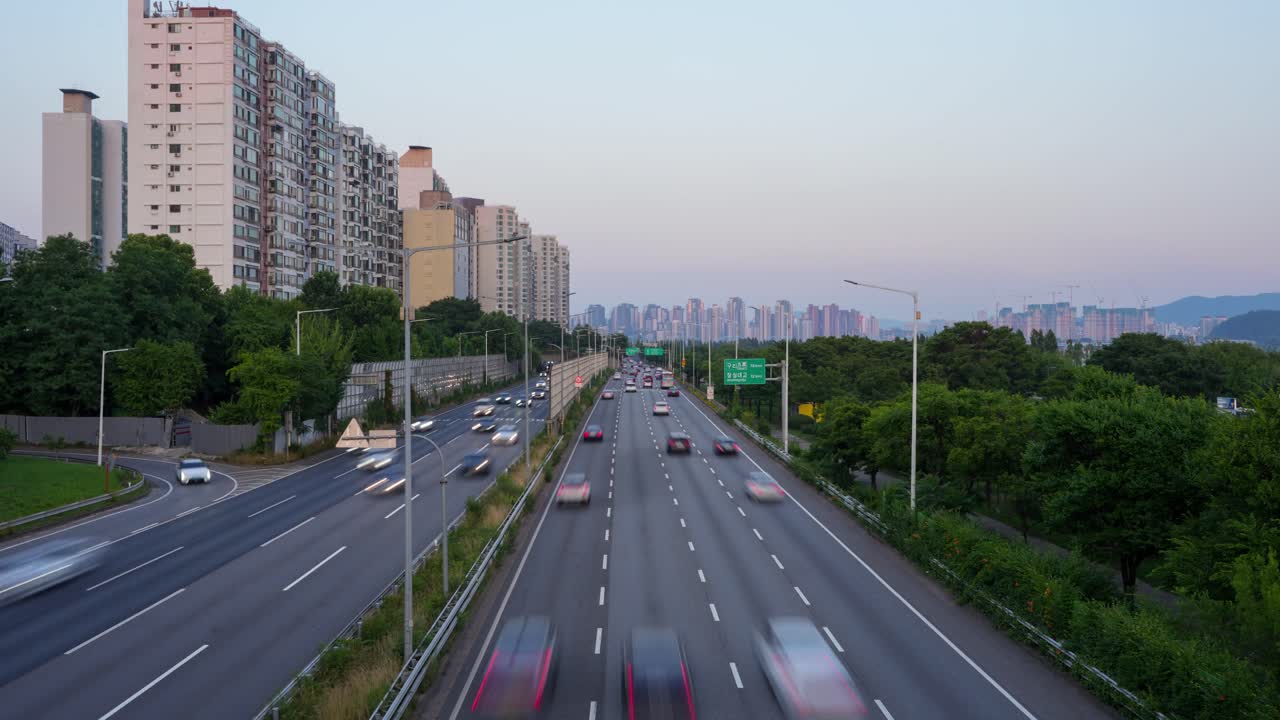 A zoom-in timelapse captures the constant flow of motion-blurred traffic along the multi-lane Gangbyeonbuk-ro expressway, lined by apartment buildings in Seoul, South Korea