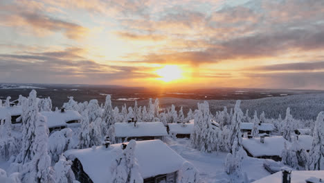 aerial view low over a snowy cabins toward arctic wilderness, sunrise in lapland