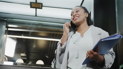 Feliz-Mujer-De-Negocios-Afroamericana-Casual-Hablando-Por-Teléfono-Inteligente-En-Ascensor,-Cámara-Lenta