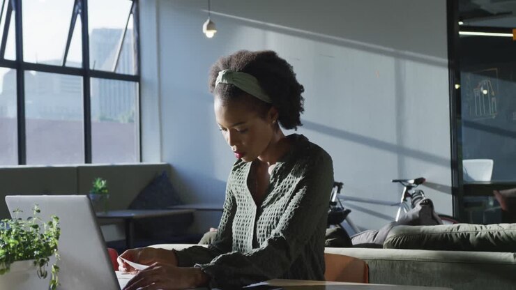 African american businesswoman sitting at table and using laptop at office