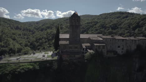 Drone's-panoramic-video-showcases-the-breathtaking-beauty-of-Castellfollit-de-la-Roca,-Spain:-medieval-village-perched-atop-a-striking-volcanic-cliff