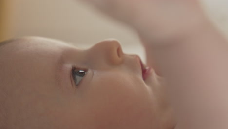 Adorable-closeup-baby's-portrait-side,-cute-eyes-nose-mouth-playful-mood-in-soft-light-bedroom