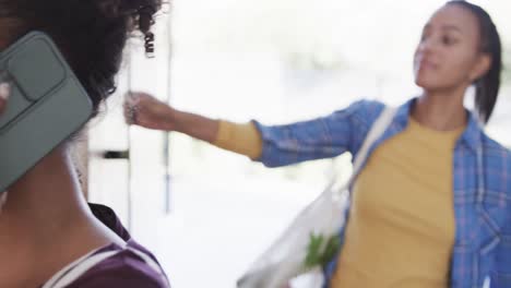 Happy-biracial-lesbian-couple-arriving-home-and-talking-on-smartphone,-in-slow-motion