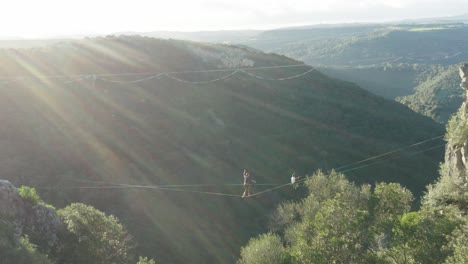 Man-Is-Walking-Along-A-Stretched-Sling---Highline-In-The-Mountains---aerial-drone-shot