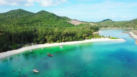 fishing boats anchoring on calm harbor with shallow water of turquoise lagoon near exotic beach with palm trees in thailand