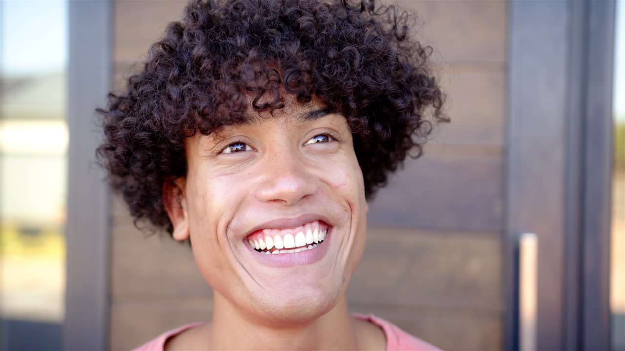 Giovane uomo sorridente con i capelli ricci che guarda in alto, sentendosi felice e appagato