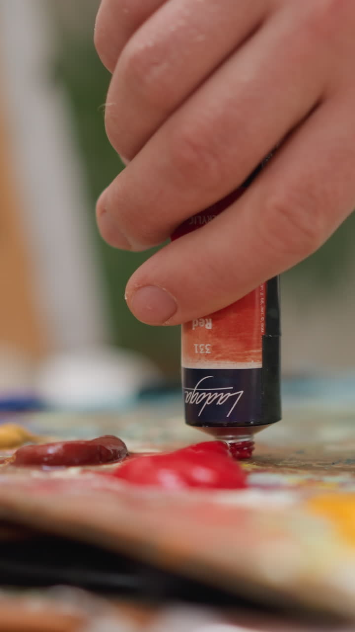 el artista exprime la pintura en la paleta en el estudio de primer plano. el hombre artístico prepara el pigmento acrílico rojo para dibujar en la tienda. el maestro de arte elige el color