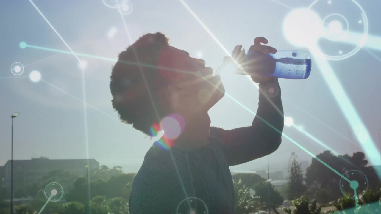 Postrun man drinking blue bottle then walking by railing while sun flares and tech overlaying sky