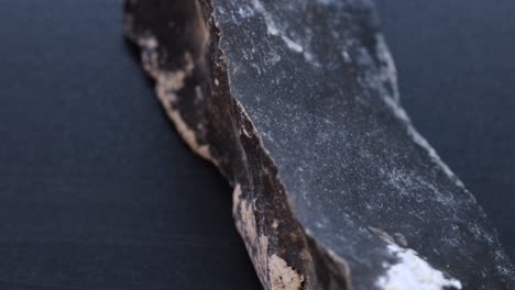 Black-flint-stone-material-used-in-ancient-times-to-make-fire-and-tools,-macro-shot-over-black-surface-with-rotating-motion