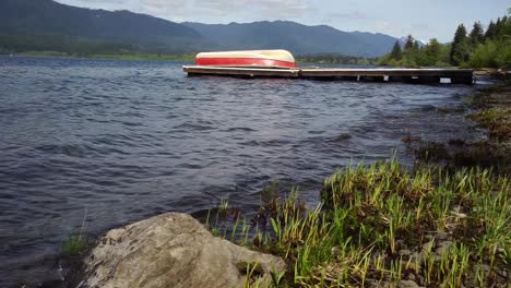 Pequeñas-Olas-Que-Lamen-Suavemente-La-Orilla-Del-Lago-Quinault,-Washington,-Un-Muelle-Flotante-Y-Un-Bote-Están-En-El-Fondo