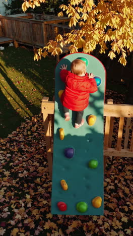 young child climbing an outdoor play wall in autumn