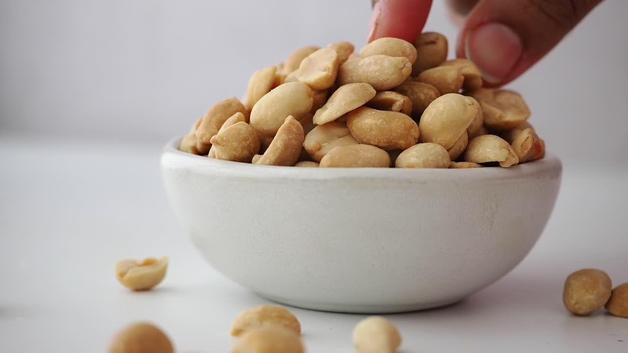 Hånd tar en ristet peanøtt fra en hvit skål