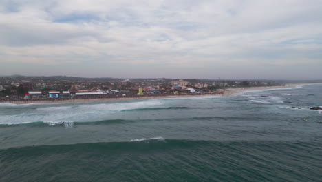 drone captures the 2025 wsl surf event at itaúna beach, saquarema, rio de janeiro. huge crowd, strong waves, surfers, tents and big screens under dramatic cloudy skies by the atlantic ocean