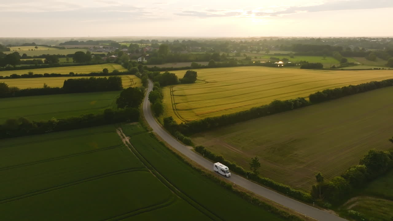 Aerial view of a motorhome driving between agricultural fields, sunny evening