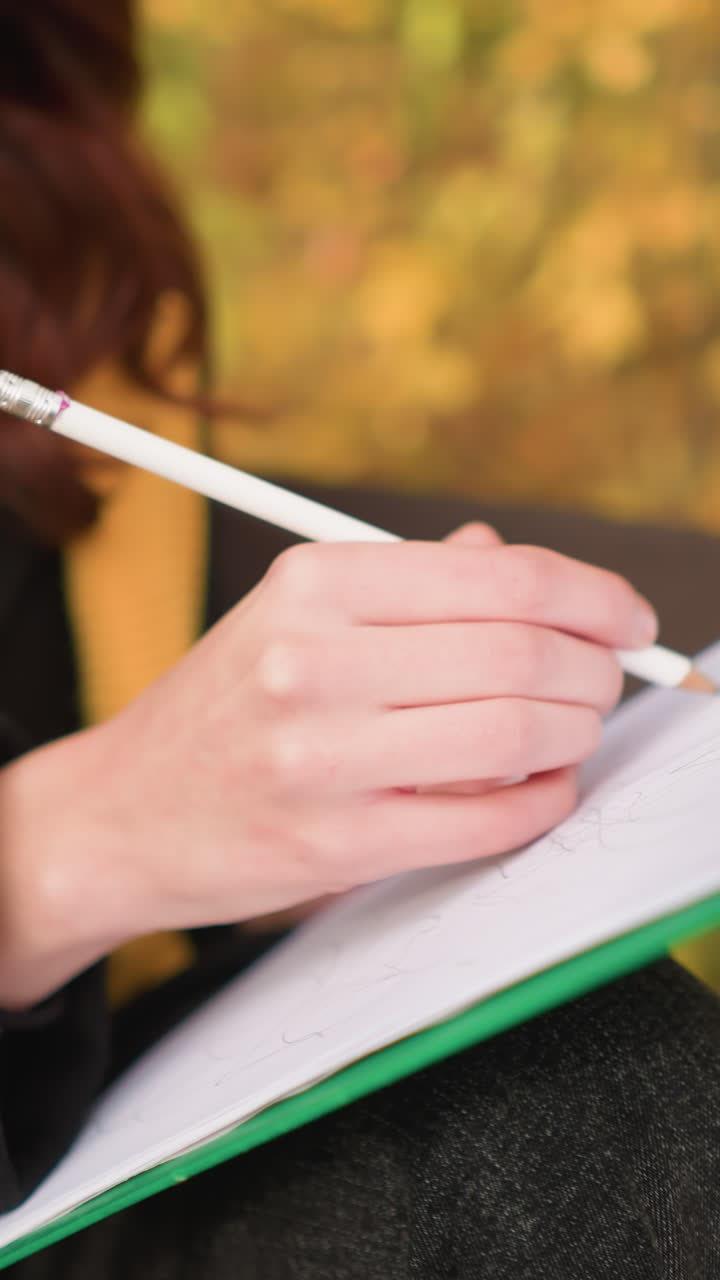 Close up of artist sketching thoughtfully on canvas with blurred autumn leaves in background, focus on artistic expression, pencil strokes, and deep concentration in serene outdoor setting