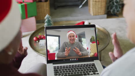 diversas amigas mayores usando una computadora portátil para una videollamada de navidad con un hombre en la pantalla