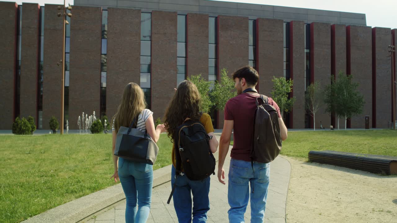 vista posterior de tres estudiantes caucásicos caminando por el campus de la universidad