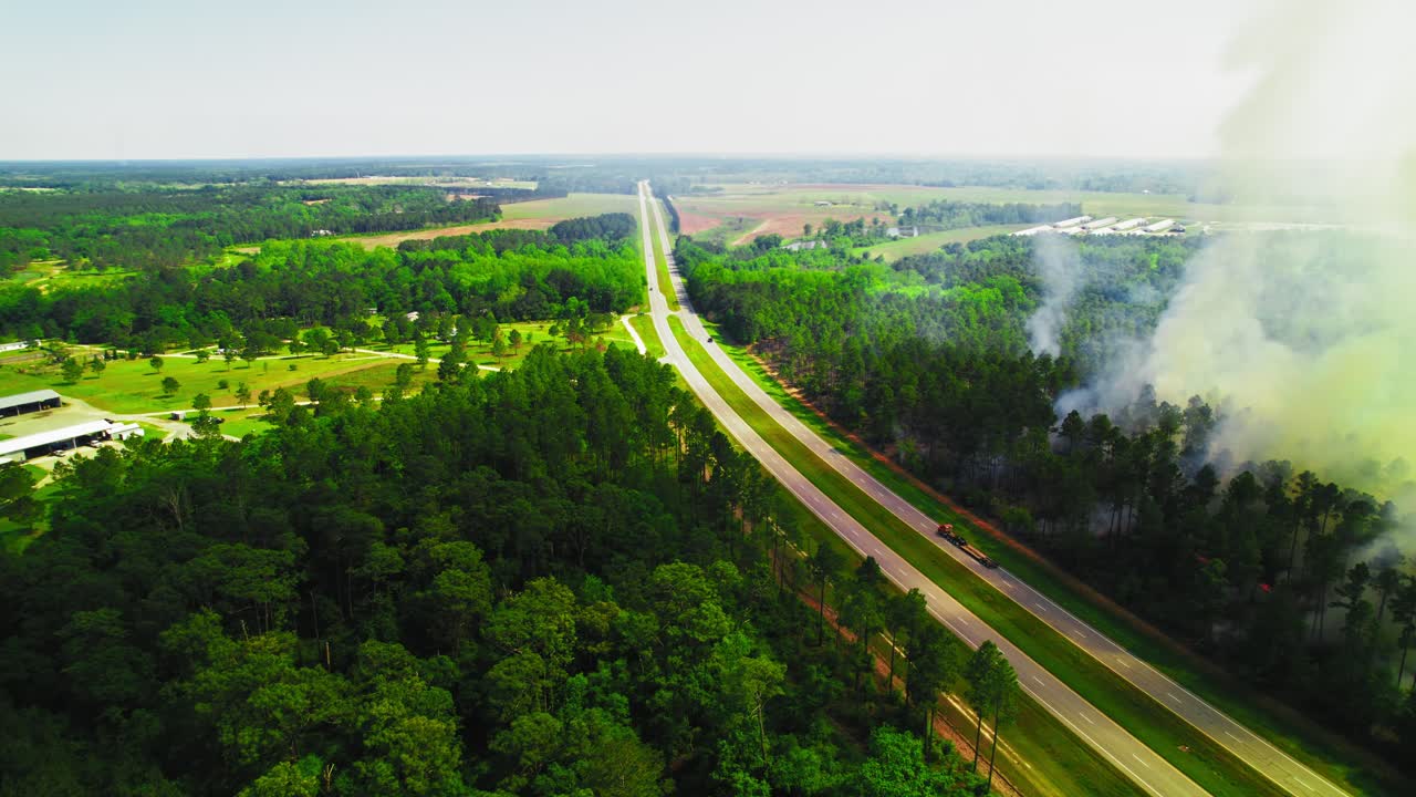Aerial view of a wildfire burning near a highway in Georgia, USA. Thick smoke plumes drift across the landscape, potentially impacting visibility and transportation.